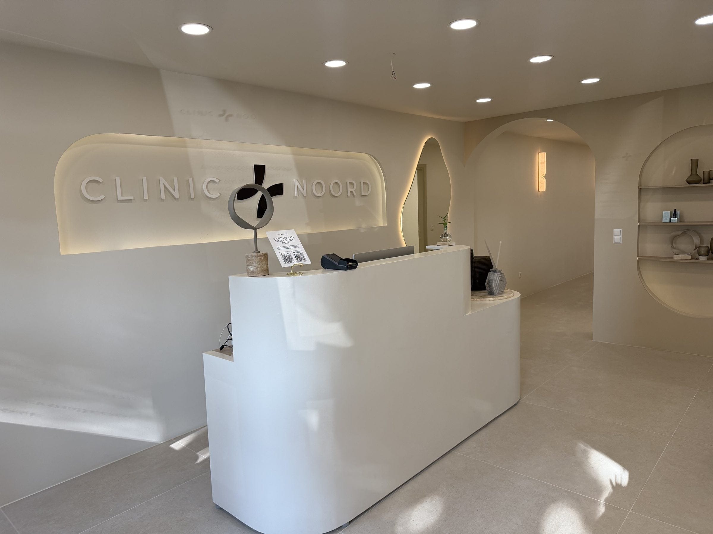 De ontvangstbalie van Clinic Noord met het verlichte logo aan de wand