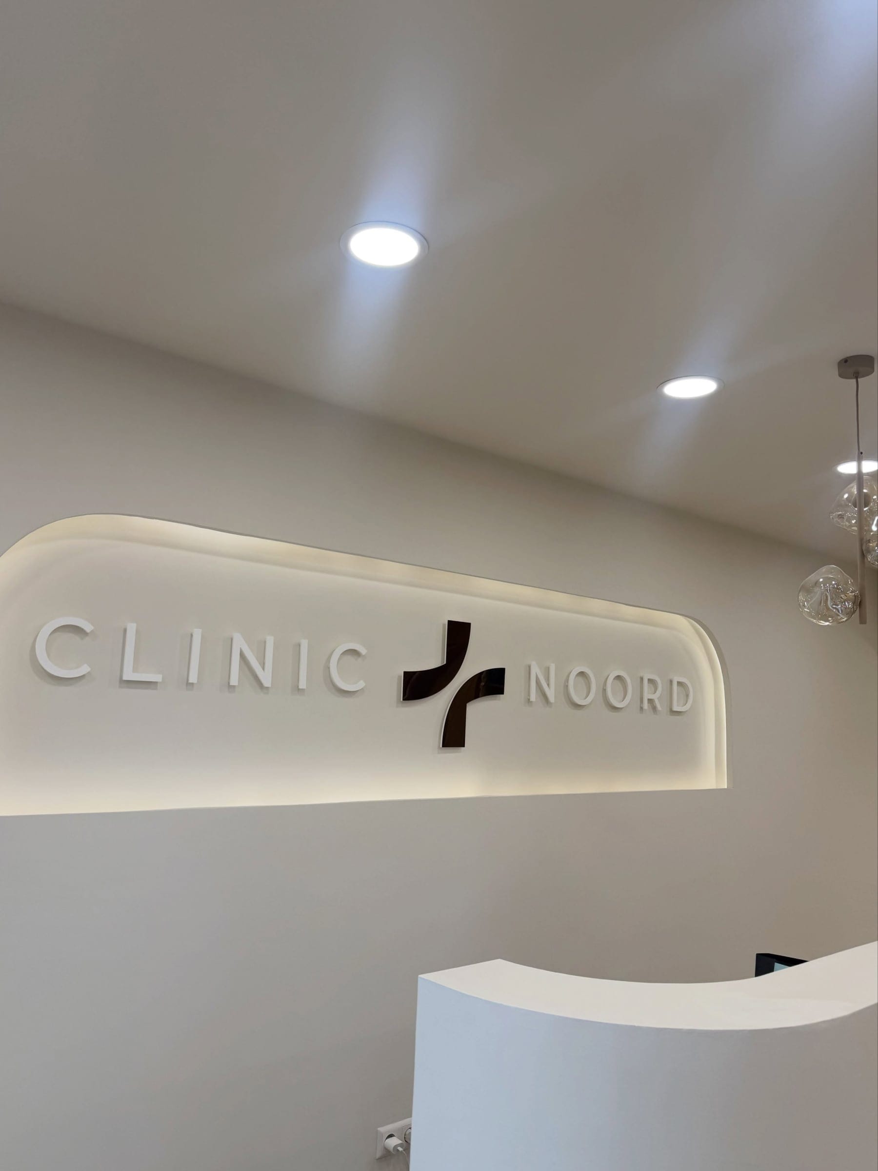 Het verlichte logo van Clinic Noord boven de ontvangstbalie